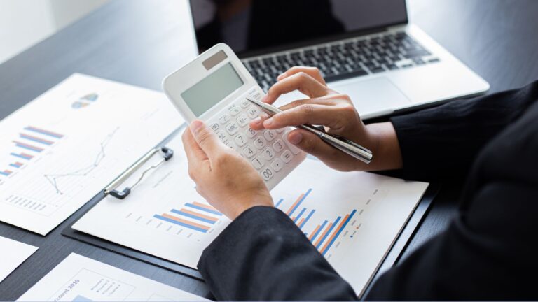 Finansų specialistas skaičiuotuvu tikrina mokesčių ataskaitas ir verslo grafikus.