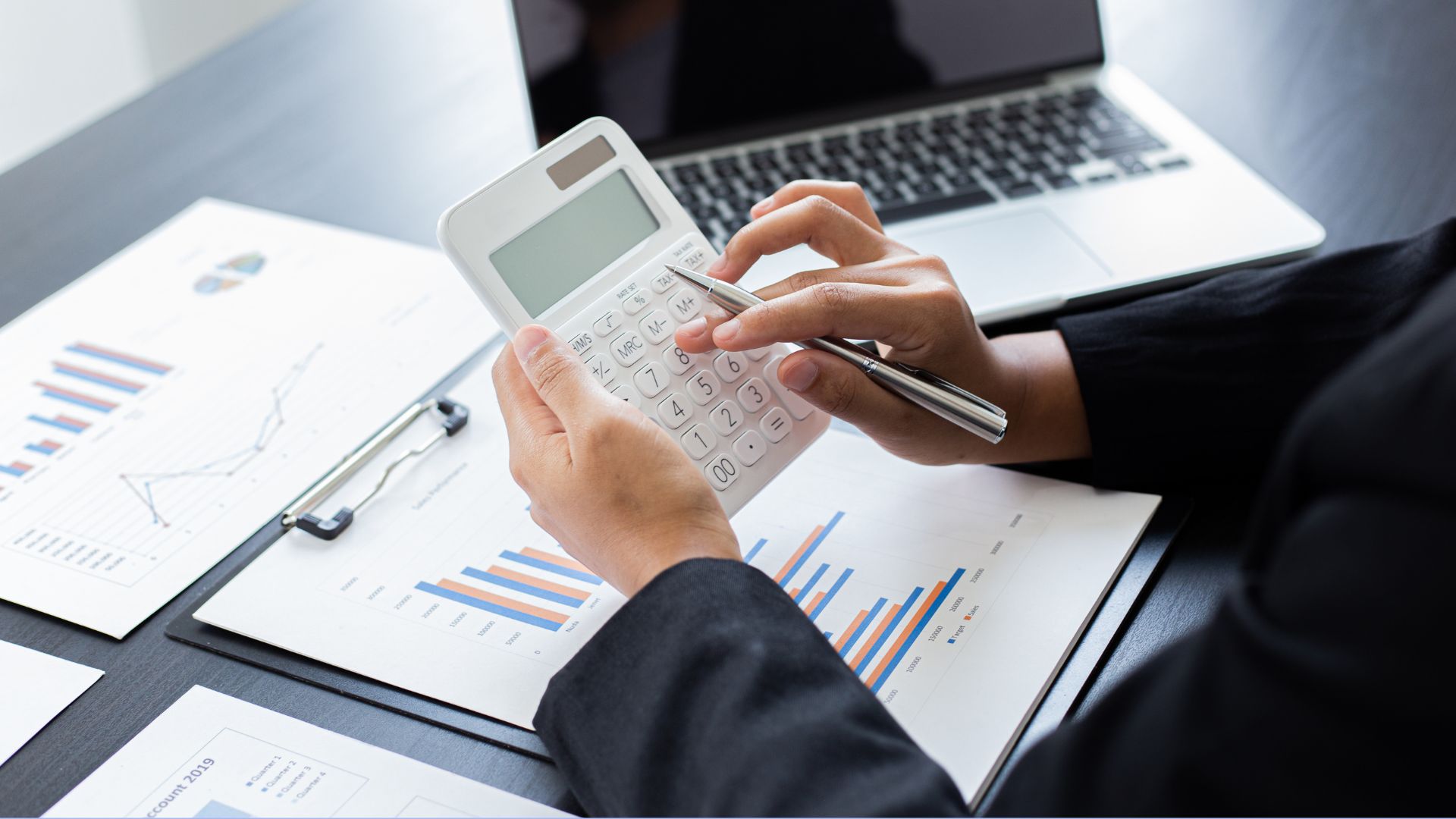 Finansų specialistas skaičiuotuvu tikrina mokesčių ataskaitas ir verslo grafikus.