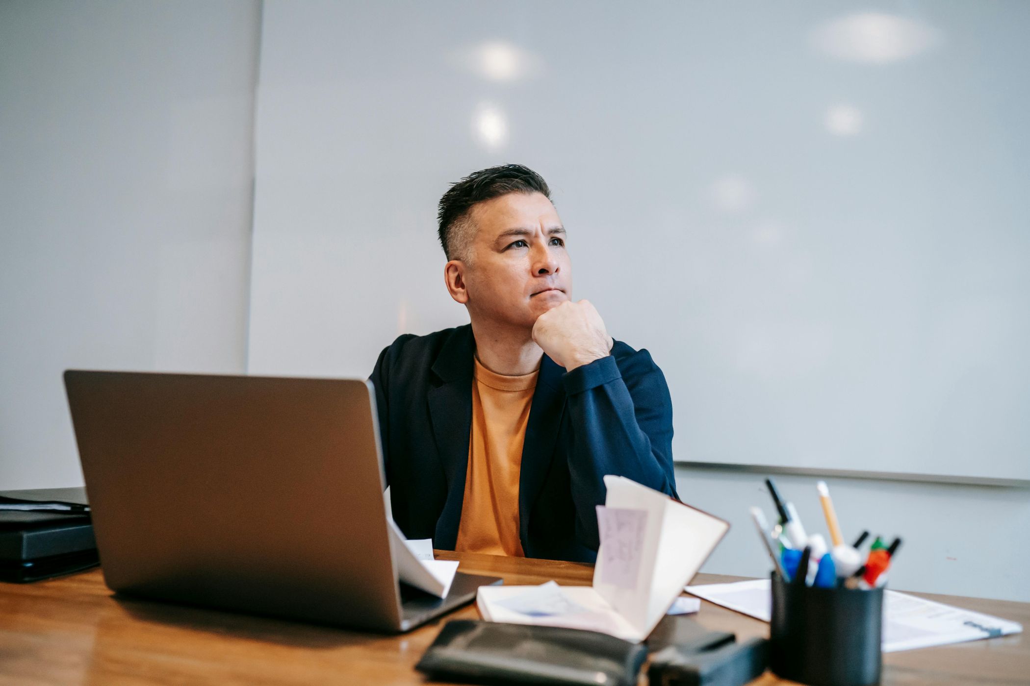 Prie stalo sėdintis ir susimąstęs vyras prie nešiojamojo kompiuterio.