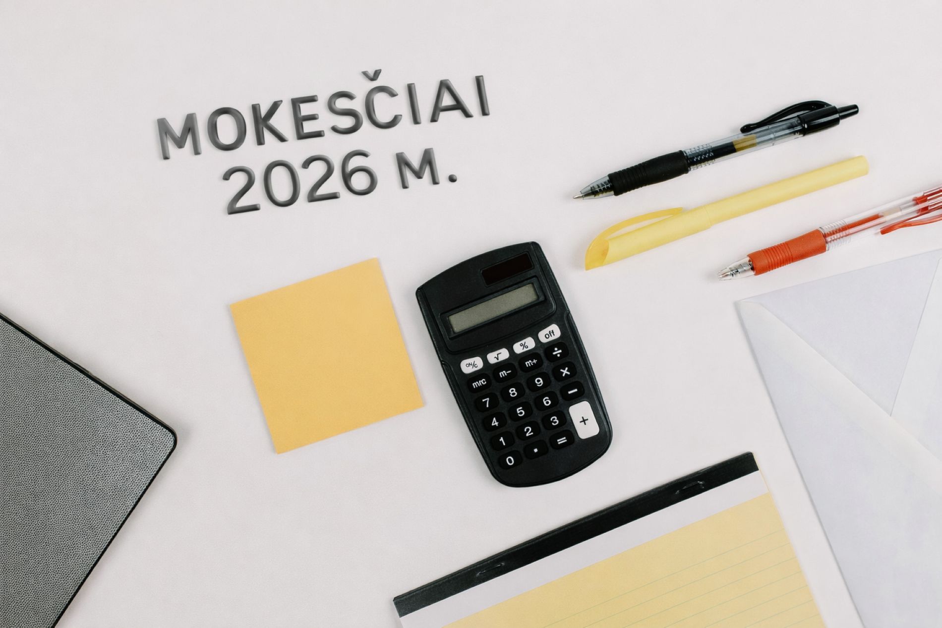 Nuotrauka baltame fone su biuro reikmenimis: juodu skaičiuotuvu centre, trimis rašikliais viršuje, geltonu lipniu lapeliu kairėje, baltu voku dešinėje ir užrašų knygele apačioje. Viršuje pilkomis raidėmis sudėtas užrašas „Mokesčiai 2026 m.“.