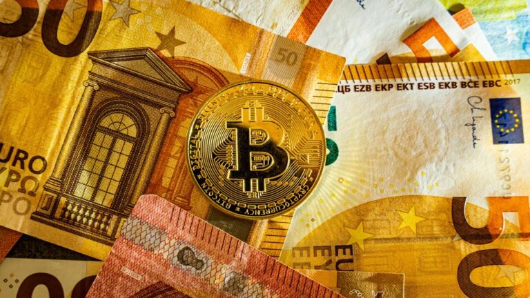 Bitcoin moneta padėta ant eurų banknotų – vizualus kriptovaliutų pavertimo į tradicinius pinigus (eurus) simbolis.