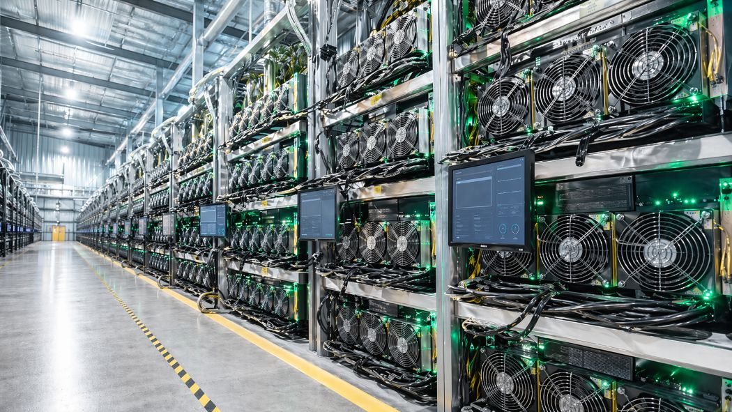 Serverių salė su ilgomis įrangos eilėmis, aušinimo ventiliatoriais, kabeliais ir indikatorinėmis lemputėmis, skirta kriptovaliutų kasimui.