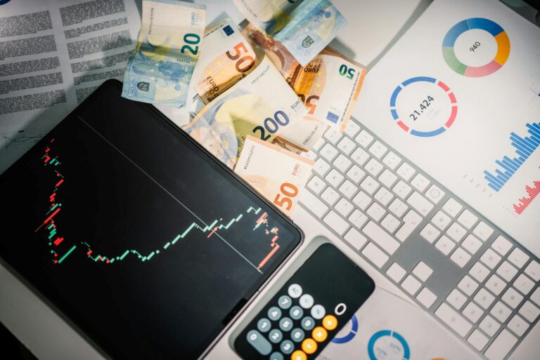 Planšetė su akcijų grafiku, euro banknotai ir skaičiuotuvas simbolizuoja investicijų pelno skaičiavimą ir akcijų pardavimo mokesčius.