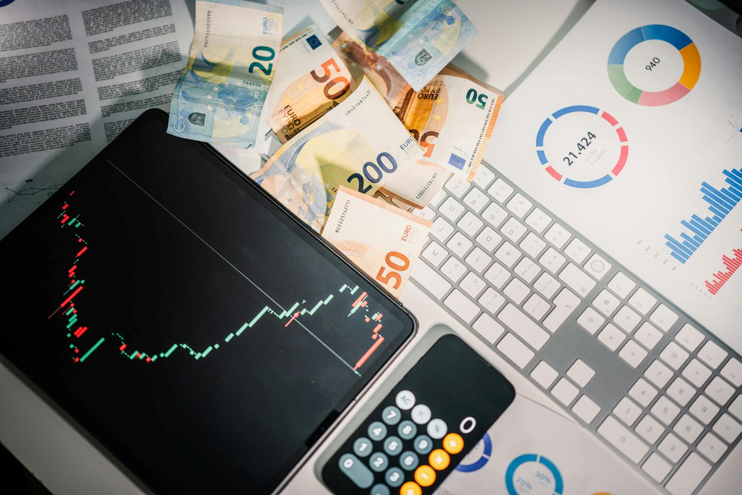 Planšetė su akcijų grafiku, euro banknotai ir skaičiuotuvas simbolizuoja investicijų pelno skaičiavimą ir akcijų pardavimo mokesčius.