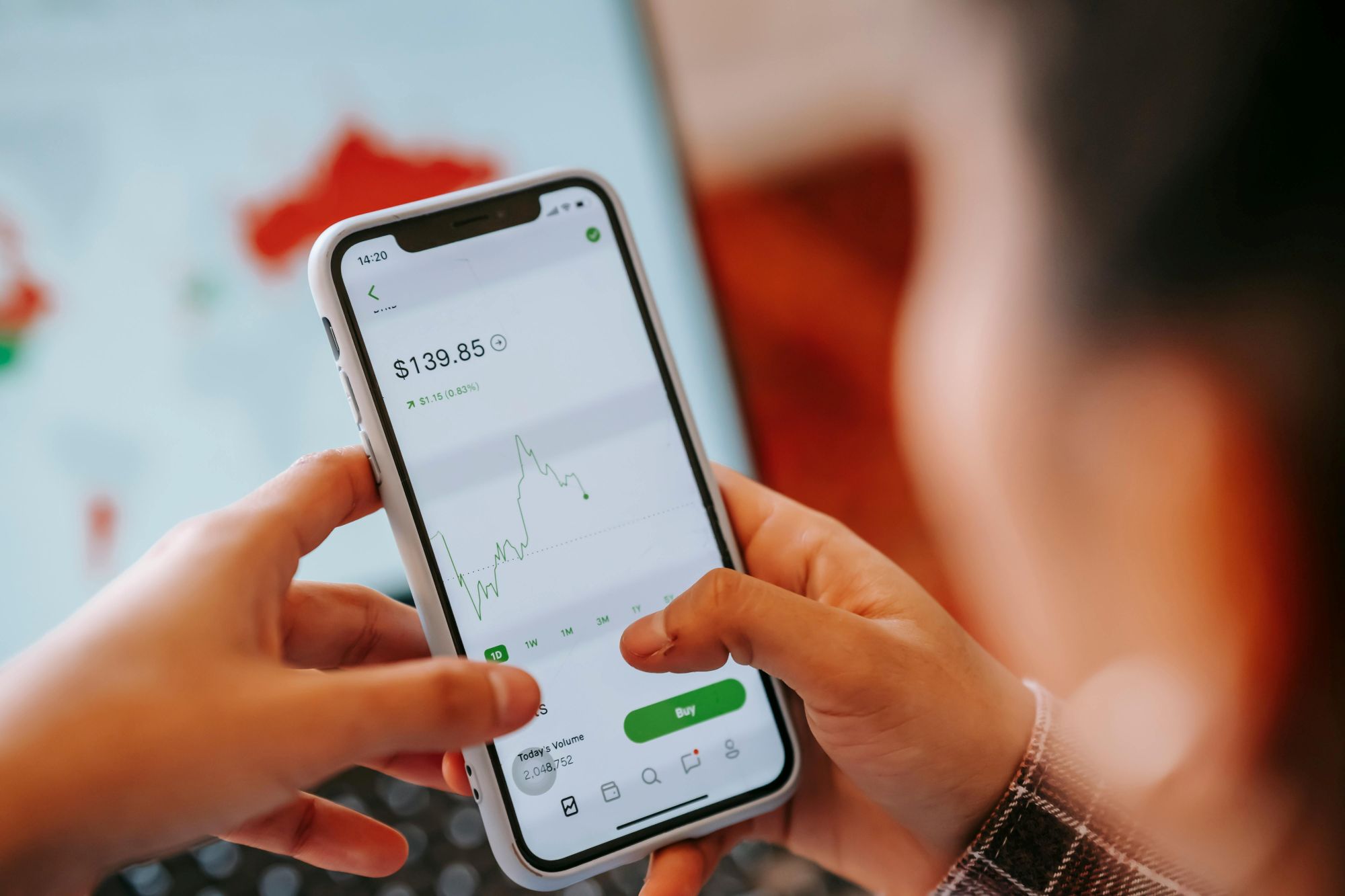 Žmogus telefone stebi investavimo programėlę ir akcijų kainų grafiką
