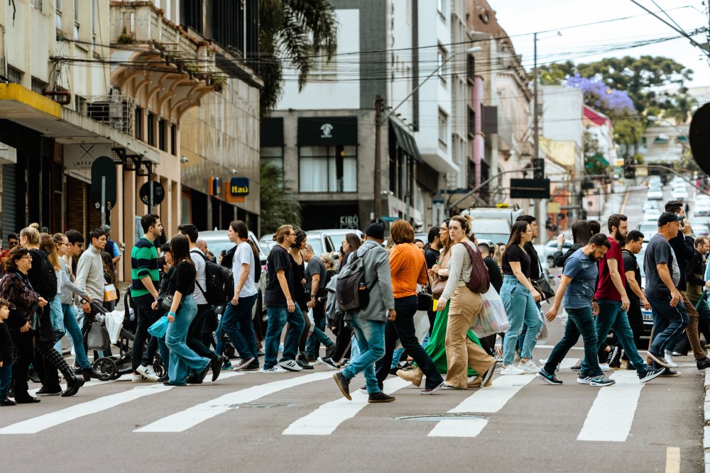 Miesto gatvėje per perėją einanti žmonių minia, iliustruojanti rinkos nuotaikos, minios elgsenos ir „contrarian“ investavimo strategijos temą.