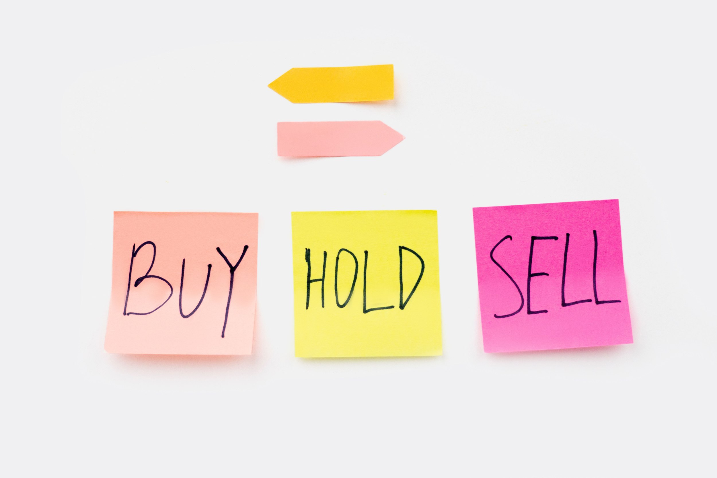 Trys spalvoti lipnūs lapeliai su užrašais „Buy“, „Hold“ ir „Sell“, iliustruojantys investavimo sprendimus ir „pirk ir laikyk“ strategiją.
