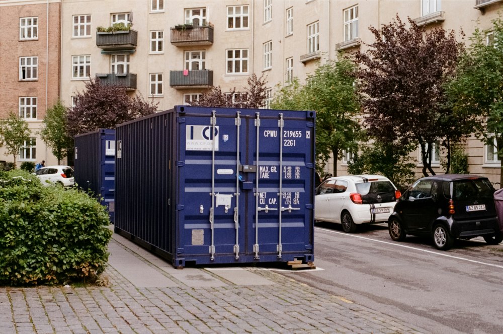 Mėlynas sandėliavimo konteineris miesto gatvėje prie daugiabučių, iliustruojantis sandėliavimo verslo ir investavimo į Public Storage temą.
