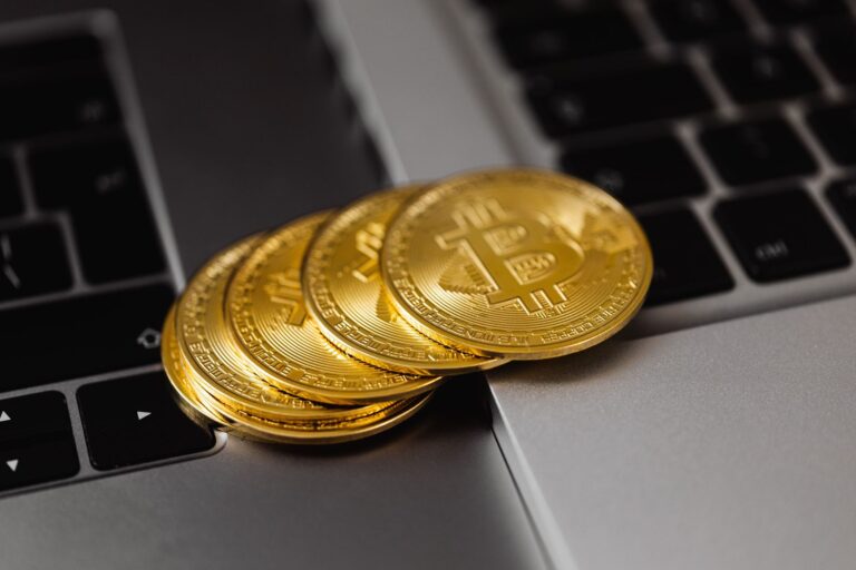 Auksinės bitkoino monetos ant nešiojamojo kompiuterio klaviatūros, iliustruojančios investavimą į bitkoiną ir su juo susijusius finansinius instrumentus.