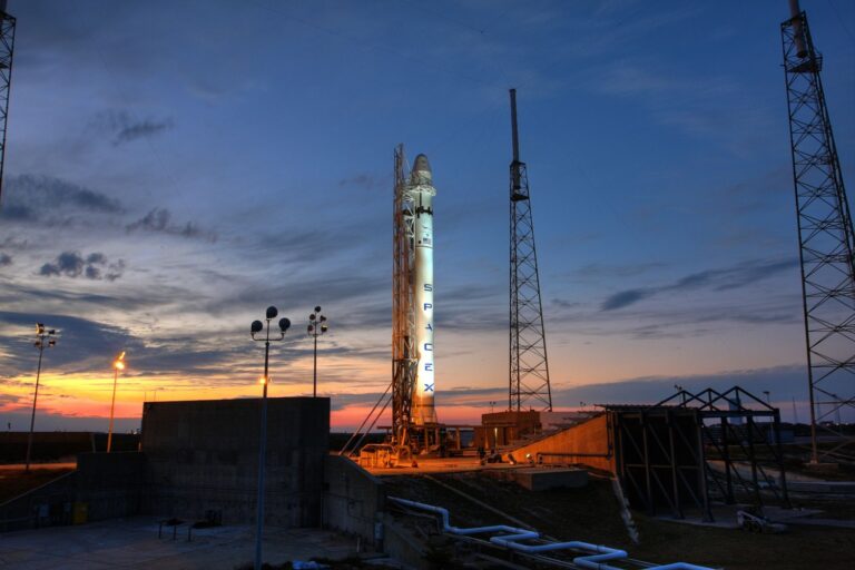 „SpaceX“ raketa paleidimo aikštelėje saulėlydžio metu, simbolizuojanti bendrovės kosmoso technologijų veiklą ir „SpaceX“ akcijas.