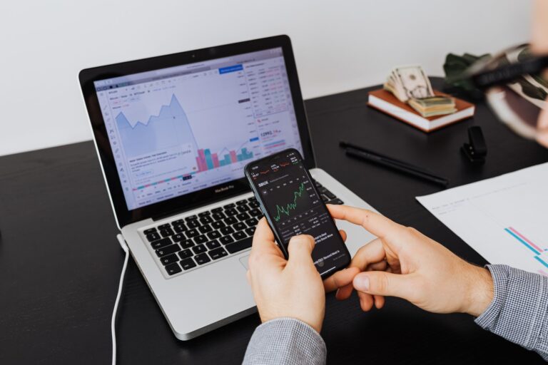 Žmogus kompiuteryje ir telefone stebi investicijas – vaizdas simbolizuoja investavimo portfelio strategijos pasirinkimą.