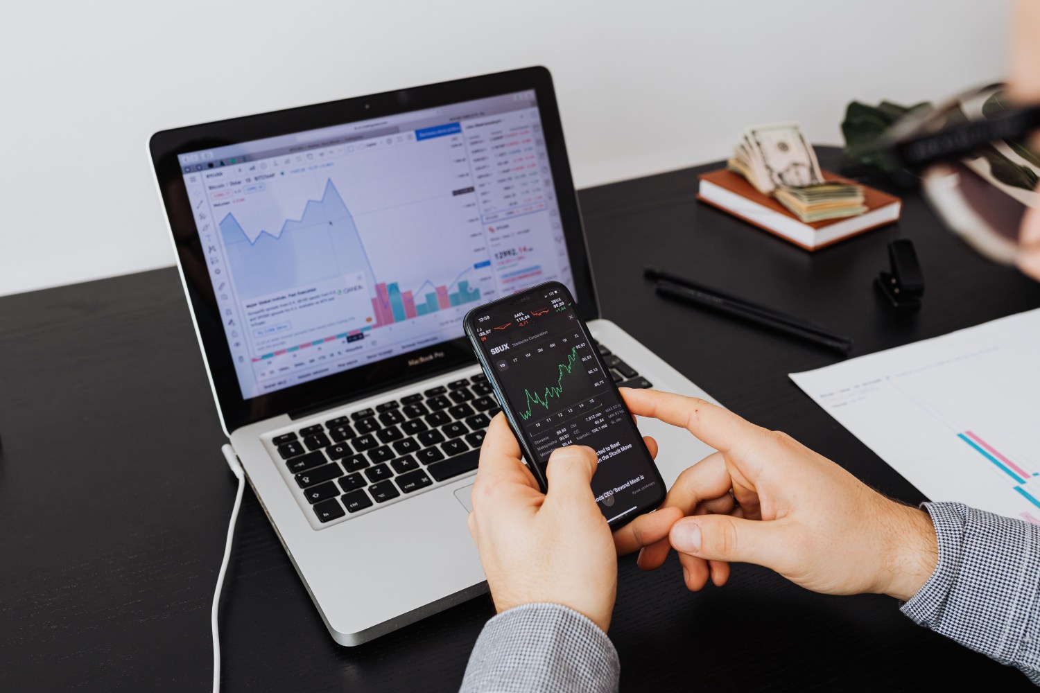Žmogus kompiuteryje ir telefone stebi investicijas – vaizdas simbolizuoja investavimo portfelio strategijos pasirinkimą.