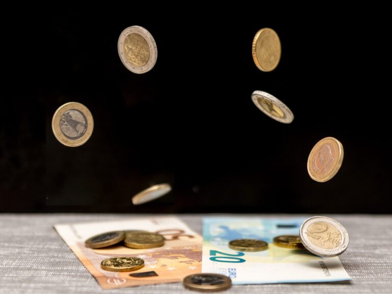 Krintančios euro monetos virš banknotų, iliustruojančios investavimo atidėjimo kainą.