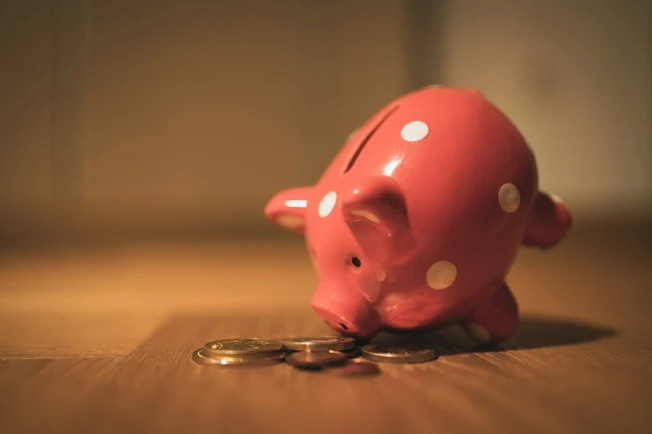 Rožinė taupyklė su monetomis, iliustruojanti taupymą ir investavimą vaiko finansinei ateičiai.