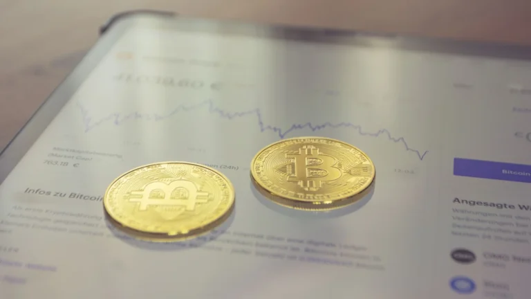 Dvi auksinės Bitcoin monetos ant planšetės ekrano su kriptovaliutos kainos grafiku. Iliustracija apie Bitcoin ETF investavimą.